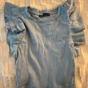 Ljusblå ribbad topp från Zara - Säljer en superfin ljusblå ribbad topp från Zara. Den har korta ärmar med volangdetaljer som ger en söt touch. Perfekt för både vardag och fest! 💙nyskick