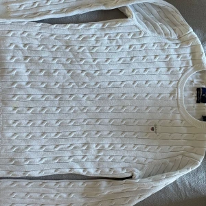 Gant  - En vit stickad tröja med kabelmönster. Tröjan har en rund halsringning och långa ärmar.   Storlek L men upplevs mer som M