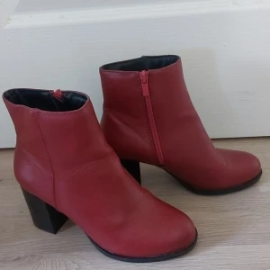 Röda stövletter med klack - Säljer ett par snygga röda stövletter i skinn. De har en 8 cm  klack och en dragkedja på sidan för enkel på- och avtagning. Perfekta för höst och vinter, och de är i helt nyskick. Passar både till vardags och fest!
