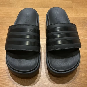 Svarta sandaler från Adidas - Säljer ett par svarta tofflor från Adidas. De är bekväma och super sköna att ha på och gå i. perfekt för sommaren. De är i nyskick och har en normal passform. Storlek 42 men funkar jättebra för liknande storlekar. Nypris: 619kr Pris: 249kr. Finns det några frågor eller funderingar är det bara att skriva.