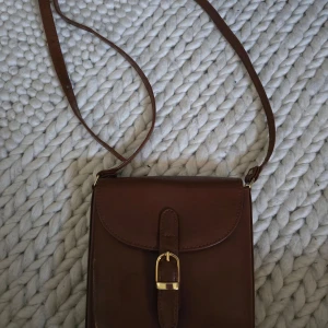 Brun väska  - Jättefin lite gammaldags brun väska med gulddetaljer. Har använts cirka 2 eller 3 gånger, fortfarande i toppskick! Står tyvärr inget märke. Pris kan förhandlas! 