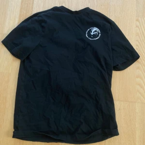 Svart t-shirt med tryck - Säljer en svart t-shirt med coolt tryck på både fram- och baksidan. På framsidan finns en liten logga på bröstet och på baksidan ett stort tryck med texten 'Turn on, Drop in, Drop out' och 'Born to Grind'. Perfekt för en avslappnad och stilren look. T-shirten är i bra skick och passar perfekt till vardags eller för en chill dag på stan.