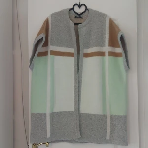 Grå och mintgrön kappa från Gina Tricot - Säljer en snygg och stilren stickad kappa/poncho från Gina Tricot i storlek XS/S. Den är grå med mintgröna, vita och bruna rutor. Perfekt för vår och höst! Den är kortärmad och har en öppen design utan knappar eller dragkedja. Superfin att ha över en tröja eller klänning. 🧥✨