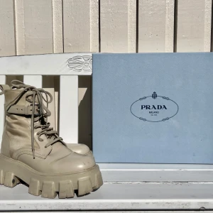 Prada monolith boots  - Säljer ett par snygga beige boots från Prada (Prada monolits boots) i storlek 37. De är i skinn och har en chunky sula som ger en cool look. jag har en av de små ”väskorna” som kommer med, den andra har jag tyvärr inte kvar. De är sparsamt använda med ytterst så skador vid tårna. de kommer med originalförpackning och alla tillbehör (förutom en av ”väskorna” som man kan sätta på skorna. Vill ni ha fler bilder får ni skriva till mig så fixar jag det! 
