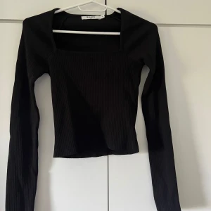 Svart ribbad topp från NA-KD - Säljer en snygg svart ribbad topp från NA-KD. Den har en fyrkantig halsringning och långa ärmar. Perfekt för både vardag och fest! 🖤