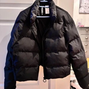 Svart pufferjacka från Gymshark - Säljer en snygg svart pufferjacka från Gymshark i storlek M. Jackan har en dragkedja framtill och är perfekt för kyligare dagar. Den har en justerbar nederkant med snörning för en bättre passform. Perfekt för både vardag och träning! Passar även S!💕