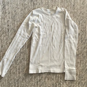 Vit ribbad långärmad tröja - Säljer en superfin vit ribbad tröja med långa ärmar. Perfekt för både vardag och mysiga hemmakvällar. Den har ett subtilt mönster som ger lite extra stil. Passar perfekt till jeans eller kjol!
