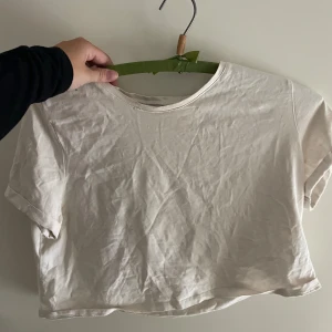 Vit croppad t-shirt - Säljer en enkel och stilren vit croppad t-shirt. Perfekt för sommardagar eller att ha under en jacka. Den är kortärmad och gjord i ett mjukt material. Passar till det mesta i garderoben!