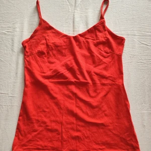 Röd linnetopp från 157 - Snygg röd linnetopp med inbyggd topp från 157 i bomull och elastan. Perfekt för varma dagar med smala axelband och en enkel design. Toppen är i en härlig röd färg som verkligen poppar. 