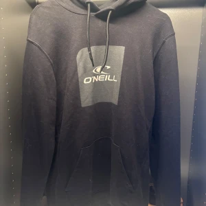 Svart hoodie från O'Neill - Säljer en stilren svart hoodie från O'Neill med logga på bröstet. Den har en klassisk design med huva och känguruficka framtill. Perfekt för en avslappnad stil.