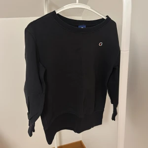 Svart sweatshirt från Champion - Säljer en stilren svart sweatshirt från Champion. Tröjan har en liten logotyp på bröstet och rund halsringning. Perfekt för en avslappnad look.