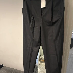 Svarta Mango  kostymbyxor - Snygga svarta kostymbyxor med en klassisk design. Byxorna har en rak passform och är perfekta för en stilren look. De har en diskret dragkedja och hällor för bälte. Passar utmärkt för formella tillfällen.