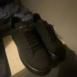 Svarta sneakers från Alexander McQueen - Snygga svarta sneakers från Alexander McQueen med en stilren design. Skorna har en solid svart färg och snörning framtill. Perfekta för en minimalistisk look.