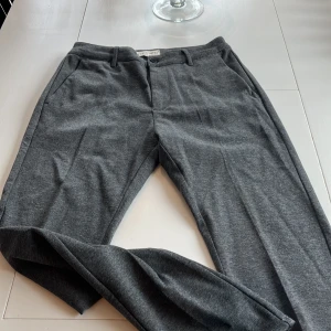 Grå kostymbyxor från Studio Total - Snygga grå kostymbyxor från Studio Total i en klassisk stil. Byxorna har en normal passform med knappar och dragkedja framtill. Perfekta för en stilren look.