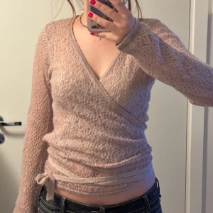 Beige omlottopp - Säljer en snygg beige omlottopp med långa ärmar. Toppen har en knytning i midjan och är tillverkad i ett mjukt material som ger en bekväm passform. Perfekt för en stilren look.