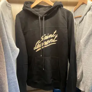 Snygg svart hoodie från Saint Laurent med deras ikoniska logga i vitt på bröstet. Tröjan är i toppskick bortsett från att den är lite smutsig på bilderna men tvättades strax efter så den är helt ren. Har haft denna i någon månad och säljer då den inte kommer till användning. Storlek S och nypris runt 7,7-8 tusen kronor! Sjukt snygg tröja passar till inprincip allt och kommer ge dig många komplimanger!