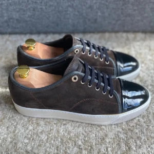 Bruna sneakers med svarta detaljer - Snygga bruna Lanvins i mocka, blanka tåhättor och snörning. Skorna har en vit sula som ger en fräsch kontrast. Perfekta för en stilren look.