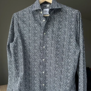 Mönstrad skjorta från Oscar of Sweden - Oscar Jacobson. Slim fit, storlek 40. 100% bomull. Mycket bra skick, precis kemtvättad. Jag säljer många skjortor i samma storlek, kolla gärna på mina övriga annonser för att skapa ett paket. Axelbredd: 47 cm Längd: 76 cm  Casual skjorta, kostymskjorta, smart, mönster, oscar of sweden, prickig, prickar.