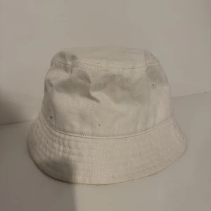 Vit bucket hat från H&M - Snygg och stilren vit bucket hat från H&M. Perfekt för sommardagar med sin enkla design och bekväma passform. Tillverkad i ett lätt och andningsbart material.