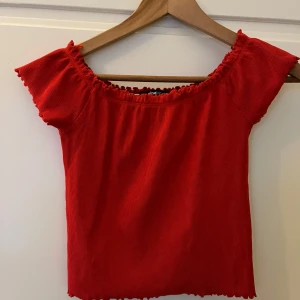 Röd ribbad topp - Säljer en snygg röd ribbad topp med korta ärmar och volangdetaljer vid ärmslut och hals. Perfekt för en trendig look! Inköpt på Ginatricot. Knappt använd, storlek M