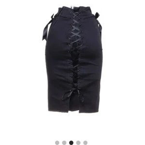 Svart kjol med snörning från Hell Bunny - Vintage svart kjol från Hell Bunny med cool snörning bak och dekorativa rosetter på sidorna. Kjolen har en tight passform som framhäver figuren och ger en edgy look. Perfekt för dig som vill sticka ut! 