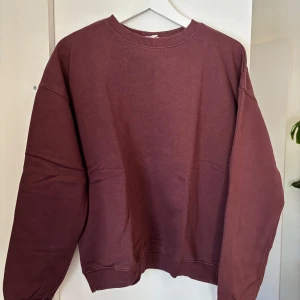 Vinröd sweatshirt - Säljer en vinröd sweatshirt med rund hals och långa ärmar. Tröjan har ribbade muddar vid ärmslut och nederkant, vilket ger en skön passform. Perfekt för en avslappnad stil.
