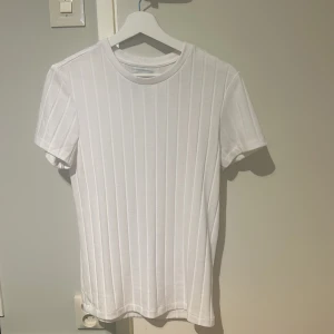 Vit ribbad t-shirt från Clayton - Säljer en stilren vit ribbad t-shirt från Clayton i storlek M men den är som storlek xs Perfekt för en enkel och fräsch look. T-shirten har korta ärmar och en rund halsringning.
