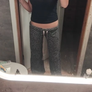 Leopardmönstrade byxor med snörning - Snygga leopardmönstrade byxor med en bekväm passform. Byxorna har en rosa snörning i midjan för justerbarhet och stil. Perfekta för en avslappnad look.