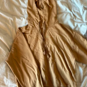 Beige hoodie från NA-KD - Säljer en snygg beige/ljusbrun hoodie från NA-KD. Den har en klassisk design med huva och dragsko, perfekt för en avslappnad stil. Materialet känns mjukt och bekvämt, vilket gör den idealisk för kyligare dagar.