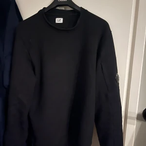 Svart tröja från C.P. Company - Snygg svart tröja från C.P. Company med rund hals och en cool detalj på ärmen. Perfekt för en stilren look. Passar bra till både jeans och chinos.