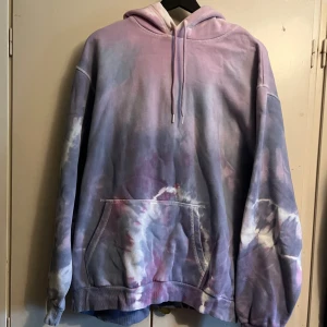 Tie-dye hoodie - Säljer en cool tie-dye hoodie från HM i lila, rosa, och blå nyanser. Den har en klassisk känguruficka och justerbar huva. Perfekt för en avslappnad stil. Materialet är en blandning av bomull och polyester. Använd fåtal gånger.