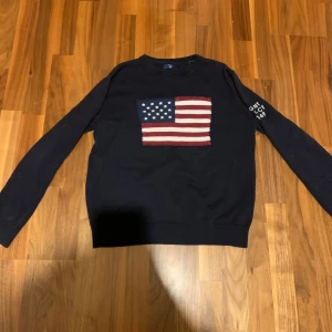 Mörkblå tröja med amerikansk flagga från Gant - Säljer en mörkblå tröja från Gant med en stor amerikansk flagga på framsidan. Tröjan har långa ärmar och texten 'GANT NH-CT 1949' på ärmen. Perfekt för en stilren och casual look. Nypris på en sån här är cirka 1299 mitt pris 599 uppen för bud kom privat för mer bilder.