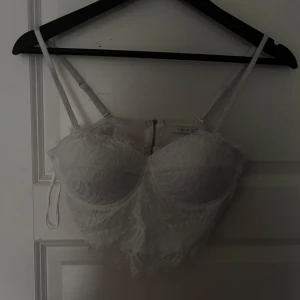 Vit spetskorsett från Amisu - Säljer en elegant vit spetskorsett från Amisu med justerbara axelband och dragkedja bak. Perfekt för att lägga till en romantisk touch till din outfit. 💫