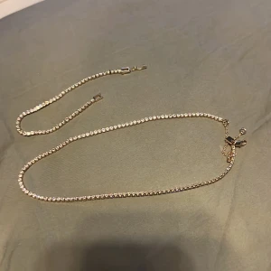 Guldhalsband och armband med glittriga stenar - Elegant set med ett guldhalsband och matchande armband, båda prydda med glittriga stenar. Perfekt för att ge en lyxig touch till din outfit.