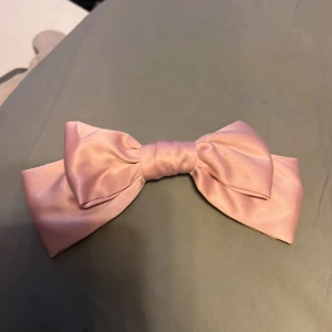 Rosa sidenrosett - Elegant rosa rosett i sidenmaterial med en praktisk klämma på baksidan. Perfekt för att ge en extra touch till din frisyr.