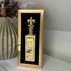 December Vanilla Parfym - Elegant parfymflaska med guldlock och dekorativ topp. Doften har toppnoter av rom, vaniljorkidé och jasmin, hjärtnoter av vanilj, läder och tonkaböna, samt basnoter av brunt socker, amber och mysk. Perfekt för den som älskar varma och kryddiga dofter.