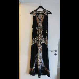 Mönstrad långklänning från Bodyflirt - Snygg långklänning från Bodyflirt med ett unikt mönster i svart, beige och brunt. Klänningen är ärmlös och har en elegant design som passar perfekt för sommarens alla tillfällen.