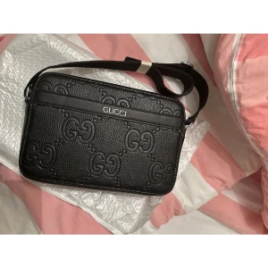 Svart axelväska från Gucci - Snygg svart axelväska från Gucci i skinn med det klassiska GG-mönstret. Väskan har en justerbar axelrem och dragkedja upptill. Perfekt för att bära med sig det viktigaste med stil.