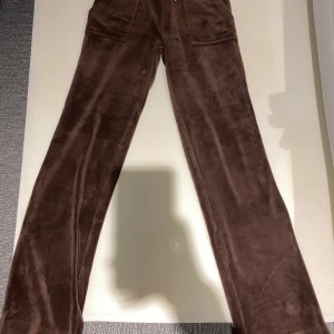 Juicy byxor brun  - Snygga bruna byxor i mjukt mockamaterial med fickor fram och bak. Byxorna har en rak passform och är perfekta för en stilren look.