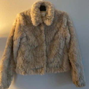 Beige pälsjacka från Vila - Säljer en fluffig och stilren beige pälsjacka från Vila. Jackan har en klassisk krage och stängs med knappar. Perfekt för att hålla sig varm och trendig under kyliga dagar.
