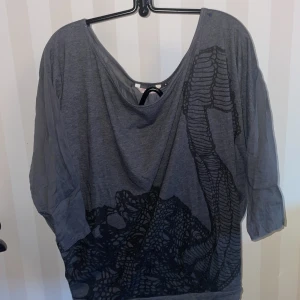 Grå topp med mönster från WE - Säljer en grå topp från WE med ett unikt svart mönster st.S passar en M också. Toppen har en lös passform och trekvartsärmar, perfekt för en avslappnad stil. Materialet är mjukt och bekvämt.