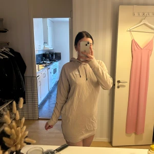 Beige hoodieklänning från Nike - Säljer en beige hoodieklänning från Nike. Den har en avslappnad passform med långa ärmar och en justerbar luva. Endast använd 1-2 gånger. Så den är som ny. 🌸