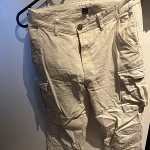 Beige cargopants - Säljer ett par beige cargopants med flera praktiska fickor och knappstängning. Byxorna har en avslappnad passform och är perfekta för en casual look.