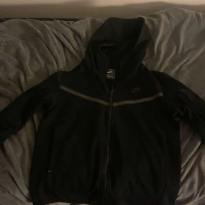 Nike Tech - Säljer en svart hoodie från Nike Tech.Perfekt för en avslappnad stil. Den har långa ärmar och en diskret logga på bröstet. Finns även byxor till den och hela dressen för 800kr men om man bara vill ha tröjan så 500kr.