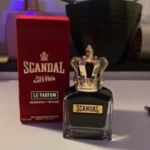Scandal Le Parfum av Jean Paul Gaultier - Elegant och djärv parfym från Jean Paul Gaultier. Flaskan har en unik design med en gyllene krona som lock och en djup svart färg. Förpackningen är röd med guldtext. Perfekt för den som vill sticka ut med en intensiv och minnesvärd doft. 2ml använt