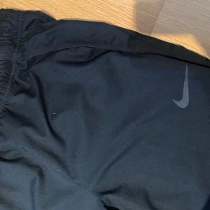 Svarta träningsbyxor från Nike - Vindbyxor/träningsbyxor från nike med en elastiskt midja. Funkar för både killar och tjejer. 