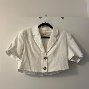 Vit croppad kavaj från Nelly - Snygg vit croppad kavaj från Nelly med korta ärmar och två knappar framtill. Perfekt för en stilren look.