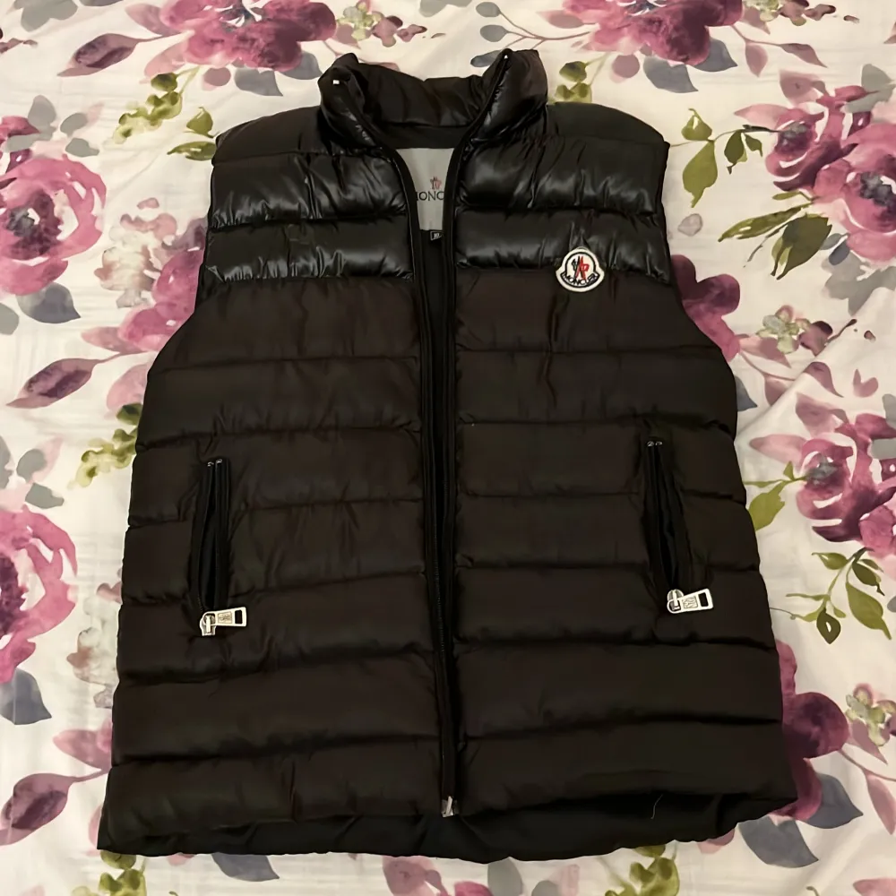 Säljer en snygg svart dunväst från Moncler med dragkedja och broderad logga på bröstet. Västen har en quiltad design och två fickor med dragkedja. Perfekt för kyligare dagar.. Muu.