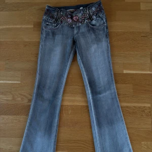 Grå bootcut jeans med broderi - Snygga grå bootcut jeans med detaljerat blommigt broderi på fickor och linning. Perfekta för en unik stil med en touch av vintage. De har en klassisk femficksdesign och en bekväm passform.