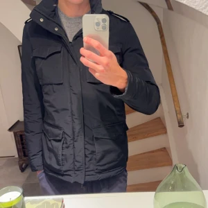 Svart jacka från Herno - SÄNKT PRIS!!                    Snygg svart field jacka från Herno. Jackan har en stilren design med knappar och dragkedja framtill. Perfekt för kyligare dagar. Skriv för fler frågor. Kan gå ner i pris vid snabb affär!